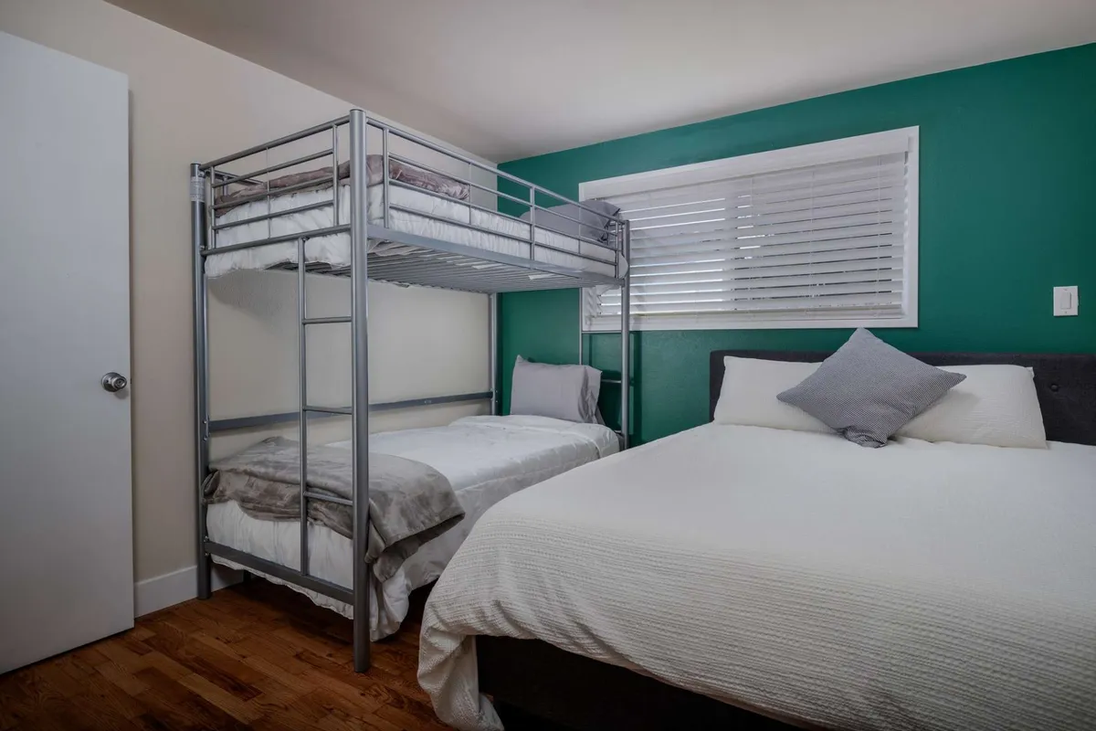 This cozy bedroom features a practical bunk bed setup alongside a double bed, complemented by a bright window with blinds. The arrangement is ideal for families or groups, offering both flexibility and comfort for memorable sleepovers or family nights.
