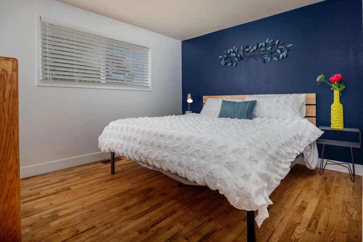A cozy bedroom highlighted by a blue accent wall and a vase of flowers beside the bed. The intimate setup and gentle lighting suggest a welcoming space for unwinding and enjoying quiet time.