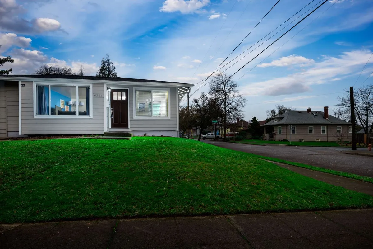 This image features the welcoming exterior of Alberta Villa, including the front door, a large window, and a green lawn. The scene is set during sunset, casting a warm, inviting light. The yard offers a glimpse into the neighborhood's community atmosphere, with space for gatherings or outdoor relaxation.