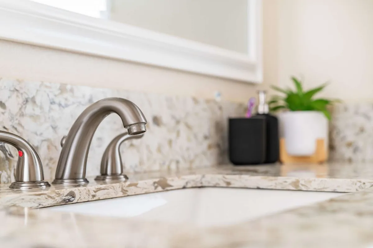 A close-up view of a sleek faucet atop a modern countertop, accented by a small plant. The scene evokes personal grooming moments and self-care rituals, suggesting fresh linens and attention to detail.