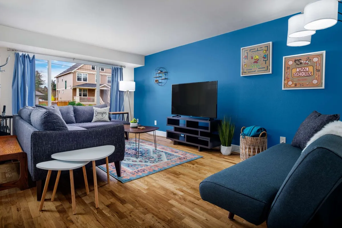 A cozy living room featuring a blue accent wall, a comfortable sofa, coffee table, television, and decorative wall art. The space is inviting and set up for relaxation, conversation, or movie nights.