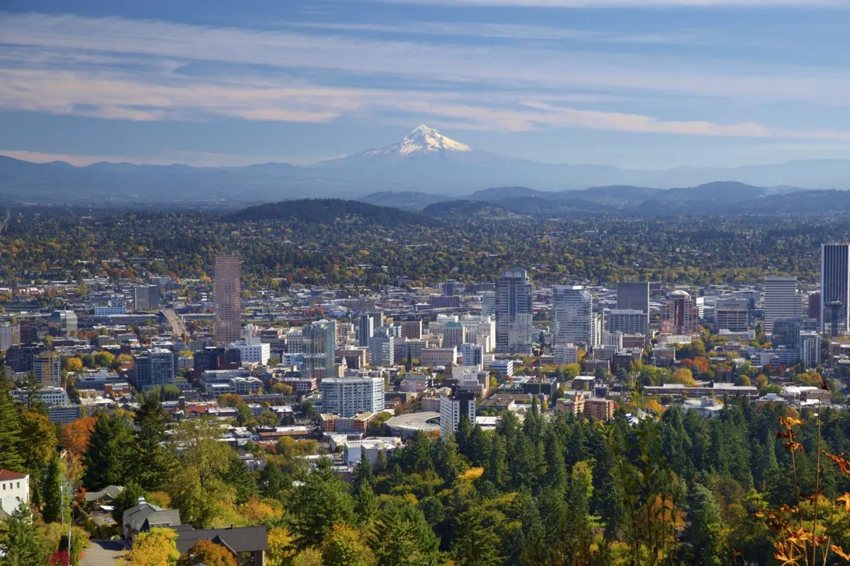 A sweeping view of the city skyline with Mount Hood in the distance, framed by autumn foliage and distant mountains. The image conveys a sense of exploration and the vibrant urban landscape accessible to guests.
