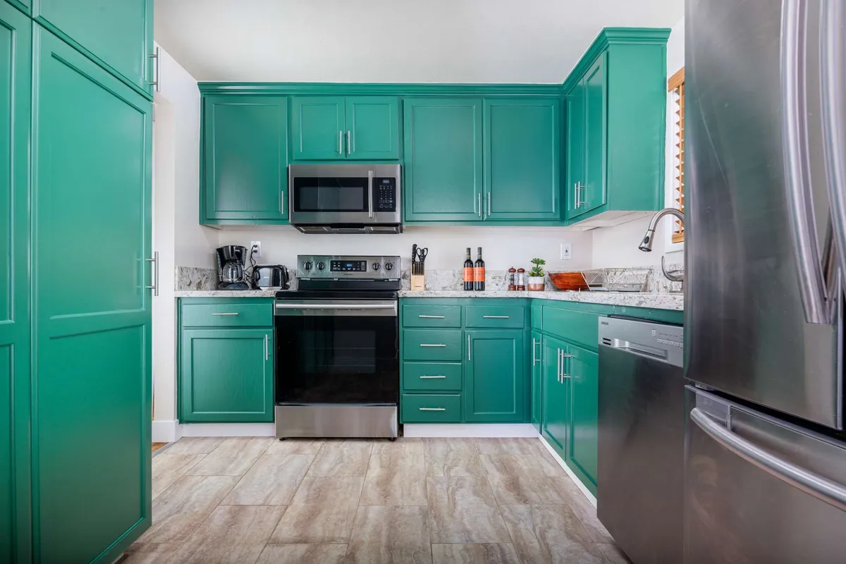 A modern kitchen with green cabinetry, stainless steel appliances, and a granite countertop. The space is well-lit and features ample room for cooking and entertaining, hinting at shared meals and bustling family activity.