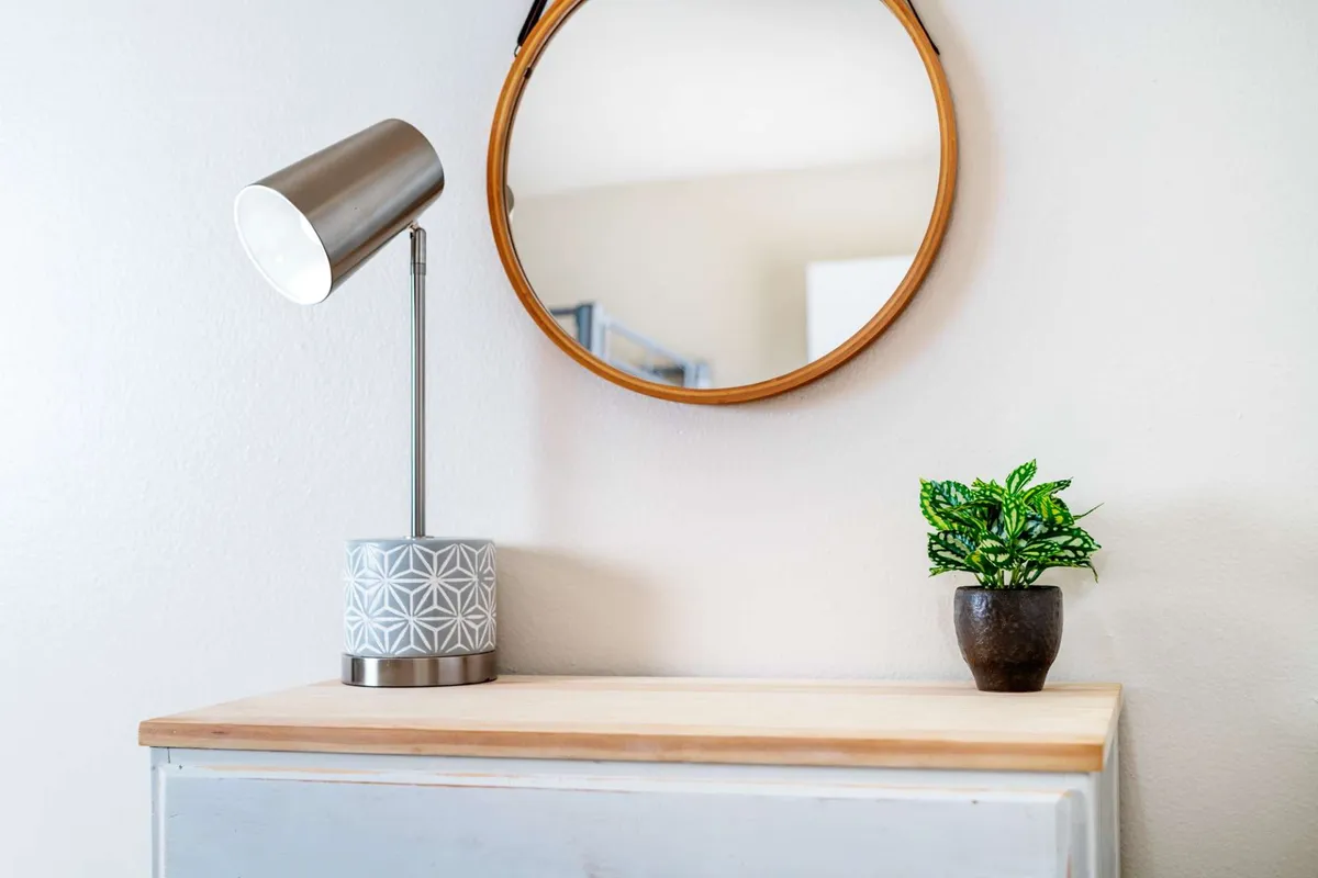 A tranquil vignette featuring a table lamp, mirror, and potted plant. Sunlight streams in, creating a warm, inviting atmosphere perfect for unwinding after a day of meetings or exploration.